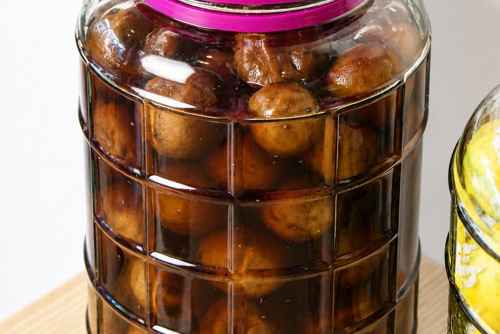 Limes months into the cure, gone dark brown in dark brine, filling a sealed glass jar.